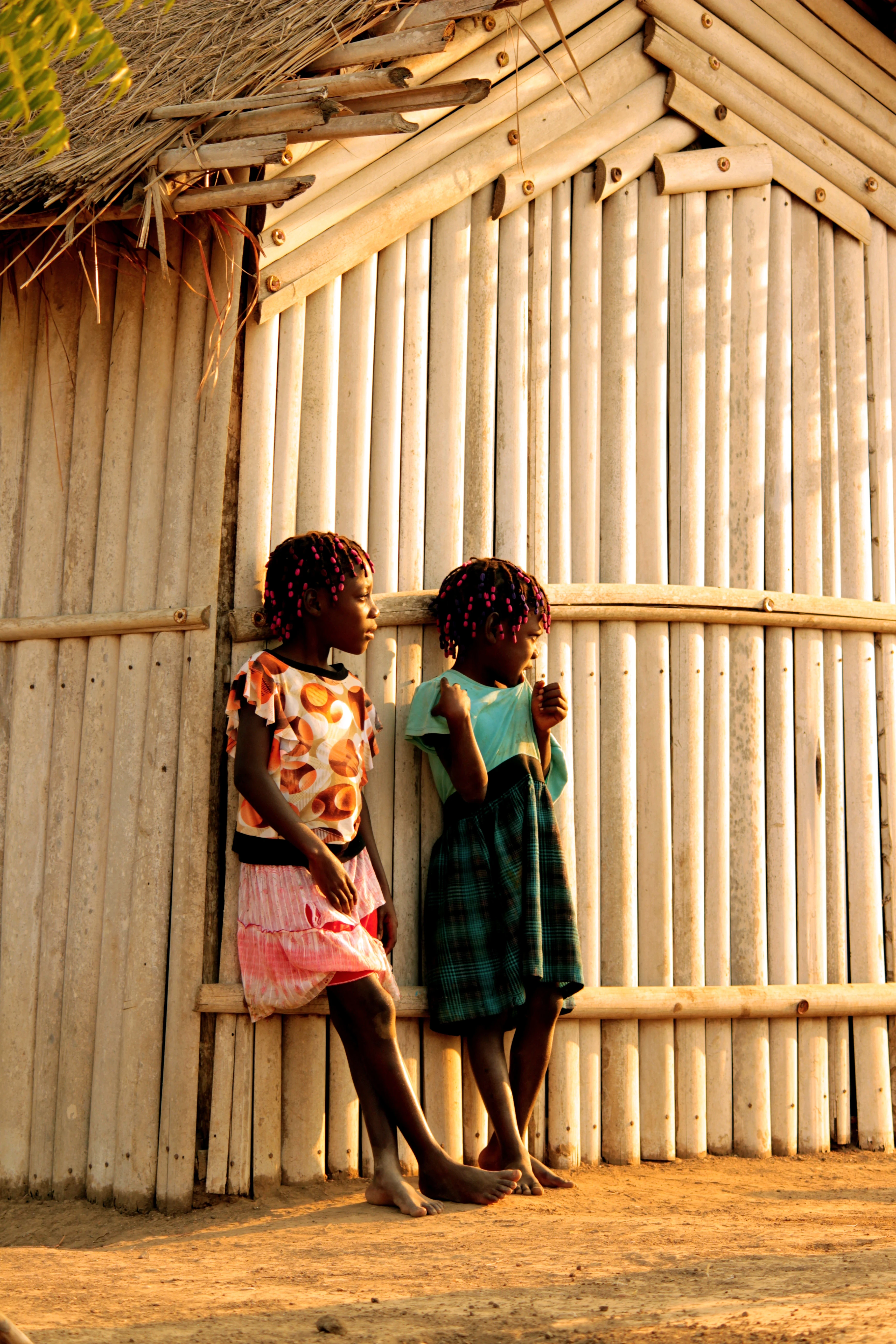 Two girls standing by a bamboo hut in warm light